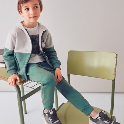 Menino de roupa desportiva senta-se numa secretária escolar com cadeira verde