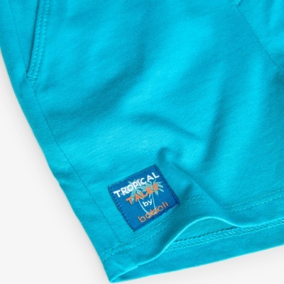 Peça de roupa azul turquesa com bolso e etiqueta azul escura com texto TRÓPICAL TALKS by babouli