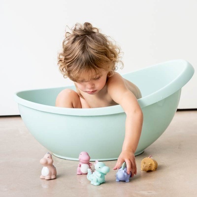 Bébé numa banheira azul-claro com brinquedos de animais coloridos no chão