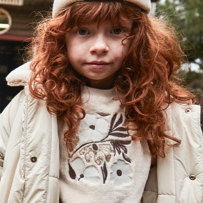 Criança com casaco acolchoado bege e camisola com padrão floral bordado