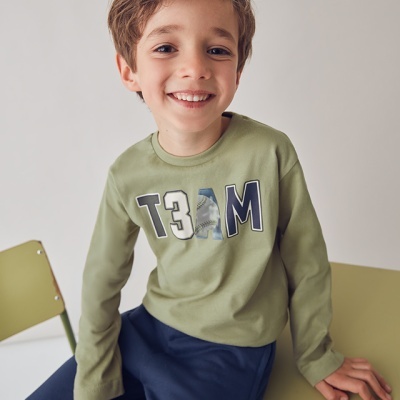 Menino sorridente com camisola verde e calças azuis sentado em cadeiras verdes