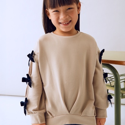 Criança com sweatshirt bege e laços pretos nas mangas