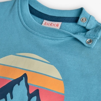 Camisola azul com estampado de montanhas e sol, fechos de pressão no ombro e etiqueta 'boboli'