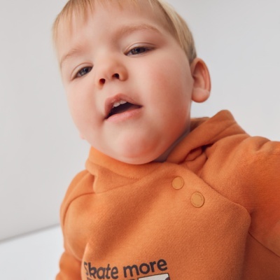 Criança de blusão laranja com estampas 'Skate more' em ambiente claro