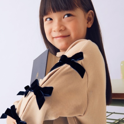 Menina com casaco bege e laços pretos segurando livro