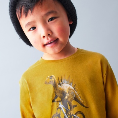 Camisola infantil amarela com estampa de dinossauro a andar de bicicleta e criança com gorro preto