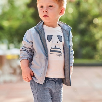 Criança ruiva com casaca cinza, t-shirt com cão e calções cinza exterior