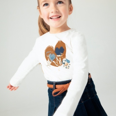 Criança com camisola branca estampada e saia azul escura com cinto castanho.