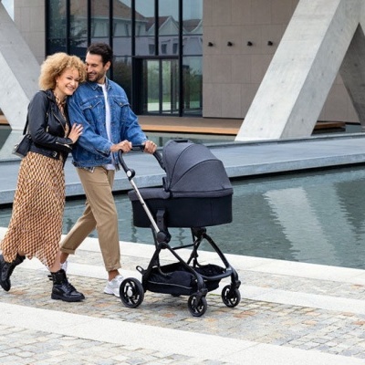 Casal a passear com carrinho de bebé preto perto de água e estruturas de betão