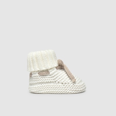 Pantufa infantil de malha branca com cadarço bege e cano dobrável em fundo cinza