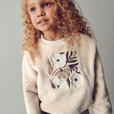 Criança com camisola creme e padrão floral, calças castanhas de veludo