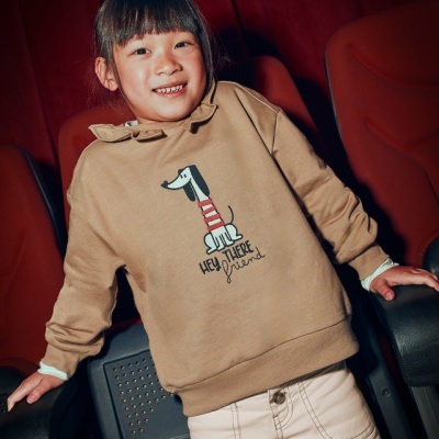 Camisola castanha com estampa de cão e frase, usada por criança em cadeiras de cinema vermelhas
