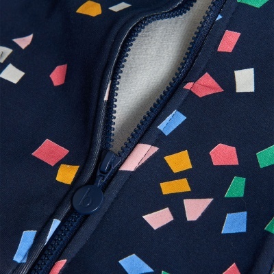 Pormenor de peça de roupa azul escura com padrão geométrico colorido e fecho éclair