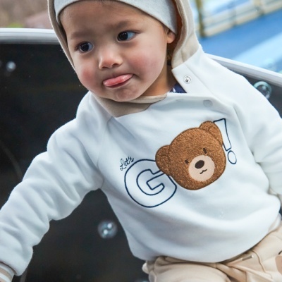 Criança de capuz branco com camisola de ursinho e calças bege no parque