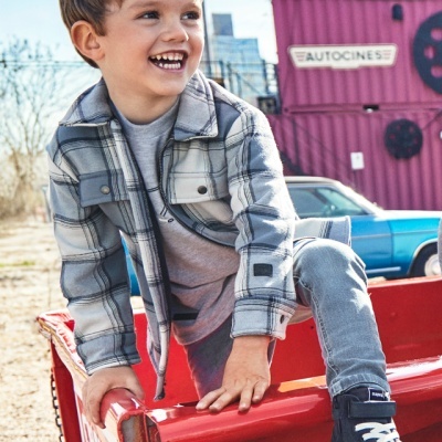 Criança com roupa casual xadrez e sapatilhas a sorrir sentada numa carrinha vermelha