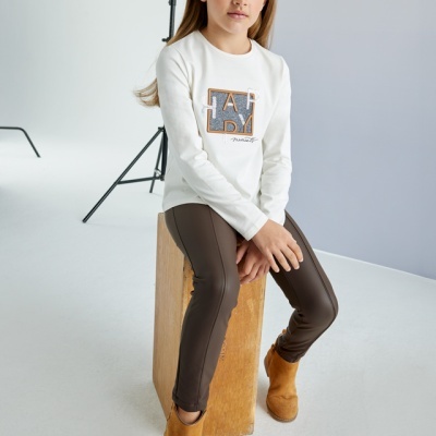 Menina com camisola branca e calças castanhas sentada numa caixa de madeira