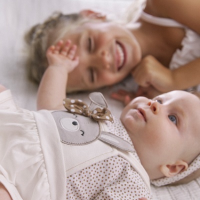 Dois bebés deitados, um com macacão branco com coelhinho bordado e padrão de bolinhas castanhas