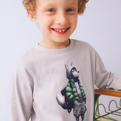 Menino loiro sorridente com sweatshirt cinzenta clara com estampa de lobo a usar casaco verde