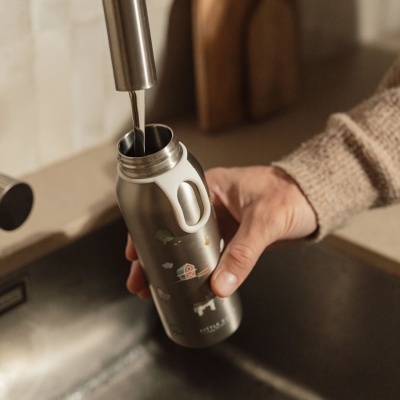 Garrafa térmica metálica decorada com imagens da quinta a ser enchida com água da torneira na cozinha