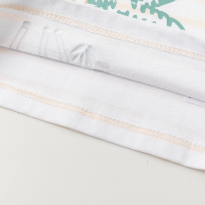 Bainha inferior de peça de vestuário branca com costuras e parte de estampado verde.