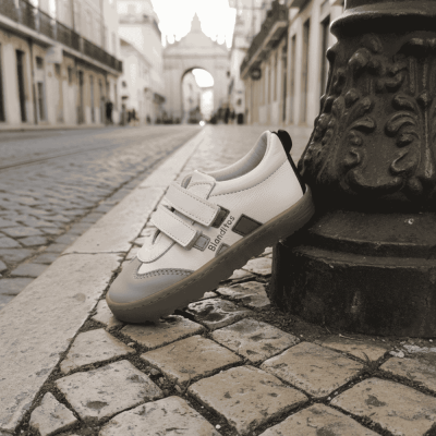 Tênis infantil branco e cinza com sola de borracha e velcro junto a poste em calçada de pedra portuguesa