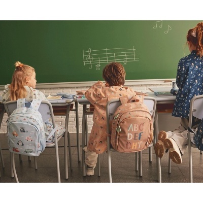 Mochilas coloridas penduradas em cadeiras de crianças numa sala de aula com quadro verde e pauta musical