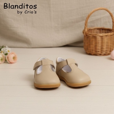 Sapatos infantis bege com fecho em tiras, cesta de verga e flores ao fundo