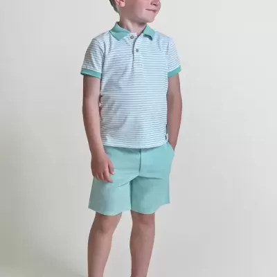 Menino com t-shirt polo branca às riscas azuis, calções verdes claros e sapatilhas brancas em fundo neutro.