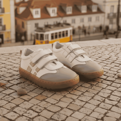Sapatilhas infantis brancas com fecho de velcro sobre calçada de pedras
