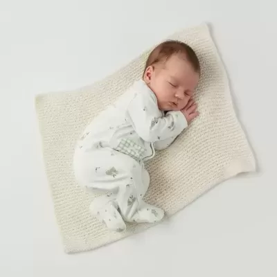 Bebé dormindo em pijama com estampa verde sobre manta tricotada branca