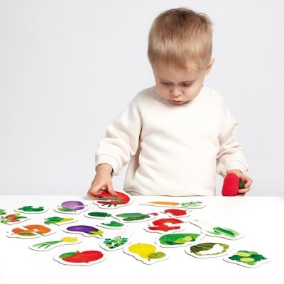 Criança com camisola branca brincando com cartas de vegetais numa mesa branca