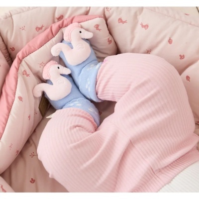 Pernas de bebé com calças rosa e meias azuis com cavalos-marinhos sobre cobertor cor-de-rosa acolchoado