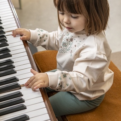 Camisola creme com estampas florais verdes e castanhas numa criança a tocar piano