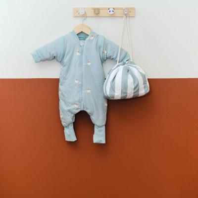Pijama de bebé azul claro com padrão de patinhos e bolsa de tecido às riscas pendurados na parede