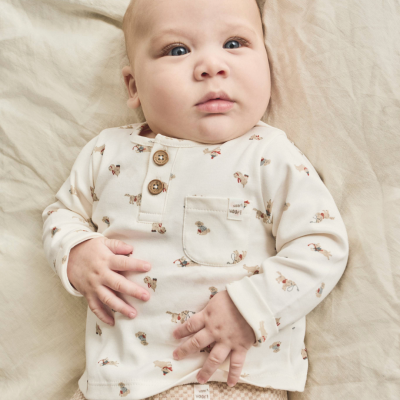 Bebé deitado com roupa creme com padrão e calças bege xadrez