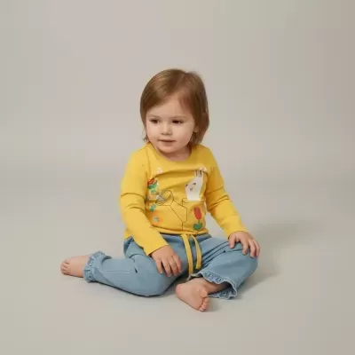 Criança com roupa amarela e azul sentada em fundo neutro.