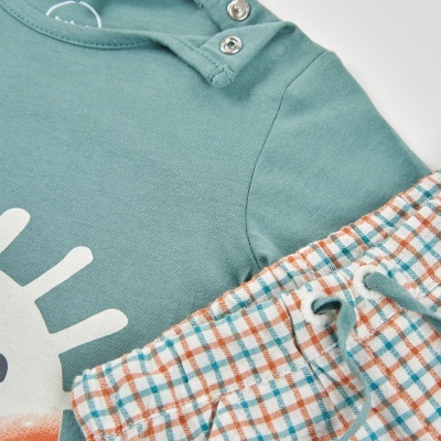 Conjunto de roupa de bebé verde e calças aos quadrados com cordão.