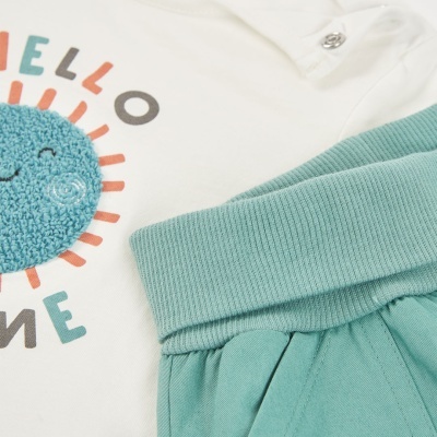 Roupa de bebé branca com sol azul e letras coloridas, e calça verde-água com punho canelado