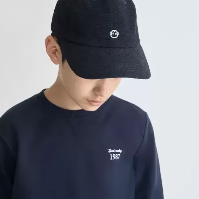 Rapaz com boné preto e camisola azul escura com texto branco