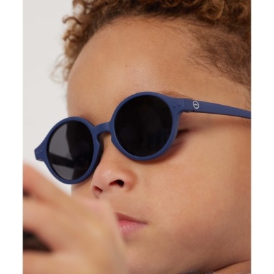 Criança com óculos de sol redondos azul escuro e camisola azul claro