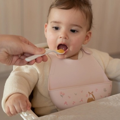 Bebé com babete rosa a ser alimentado com colher de plástico