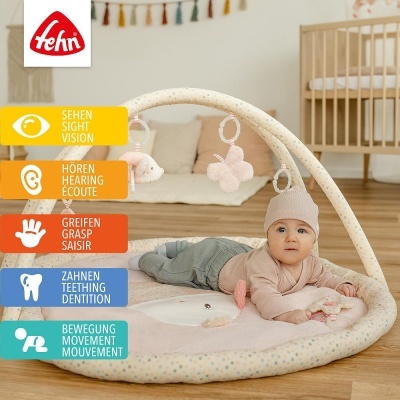 Tapete de atividades de tecido creme com pontos coloridos e brinquedos cor-de-rosa pendurados.