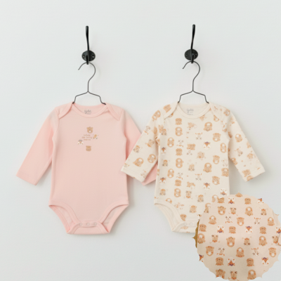 Dois bodies de bebé em algodão, um rosa com texto e pequenos desenhos, outro creme com padrão de carrinhos castanhos, pendurados em cabides pretos