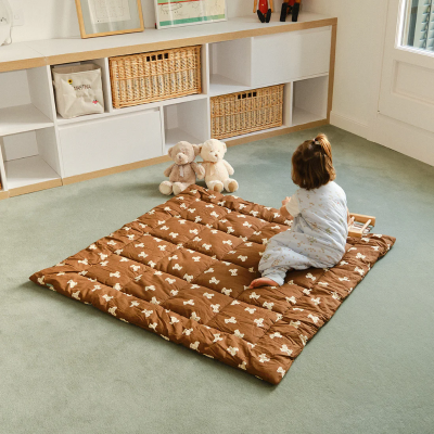 Manta almofadada castanha com padrão de ursinhos com criança sentada em cima