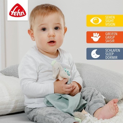 Bebé segurando brinquedo de tecido macio, sentado com almofadas ao fundo e texto multilingue sobre visão, apreensão e sono