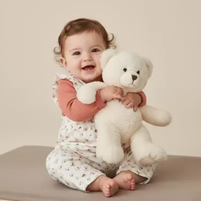 Bebé abraça urso de peluche branco sentado
