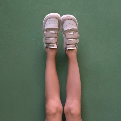 Ténis infantis creme em fundo verde com pernas de criança