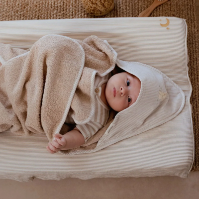 Bebé deitado em almofada riscada creme com toalha bege com capuz riscado