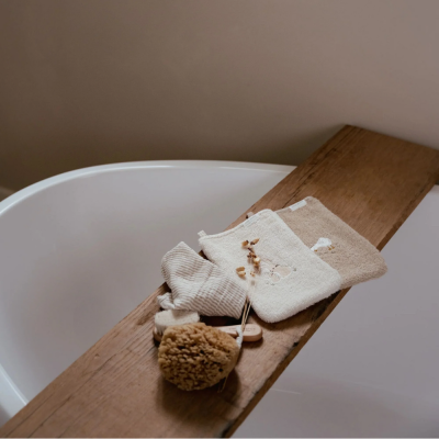 Panos e esponja natural em tábua de madeira sobre banheira branca