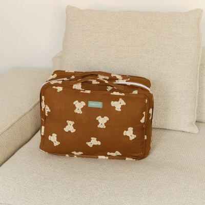 Mala castanha com padrão de ursinhos sobre sofá claro com almofada atrás